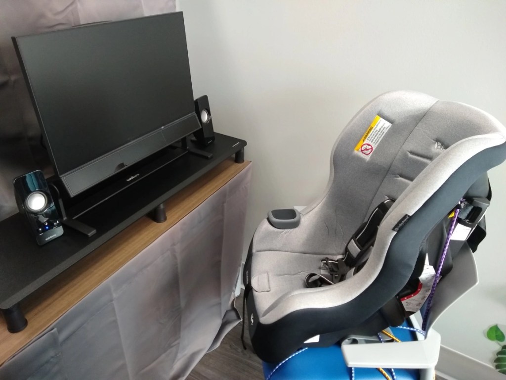 A car seat in front of a computer monitor with an eye tracker.